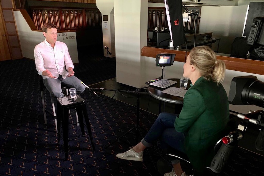 Woman sitting opposite man with microphone and TV equipment around them.