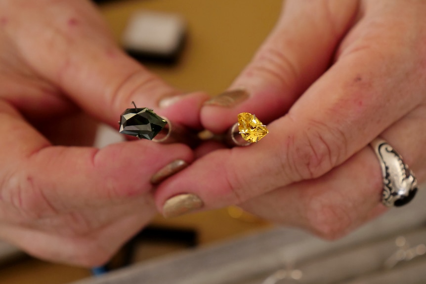 Hands holding two precious gemstones, one dark blue and one yellow.