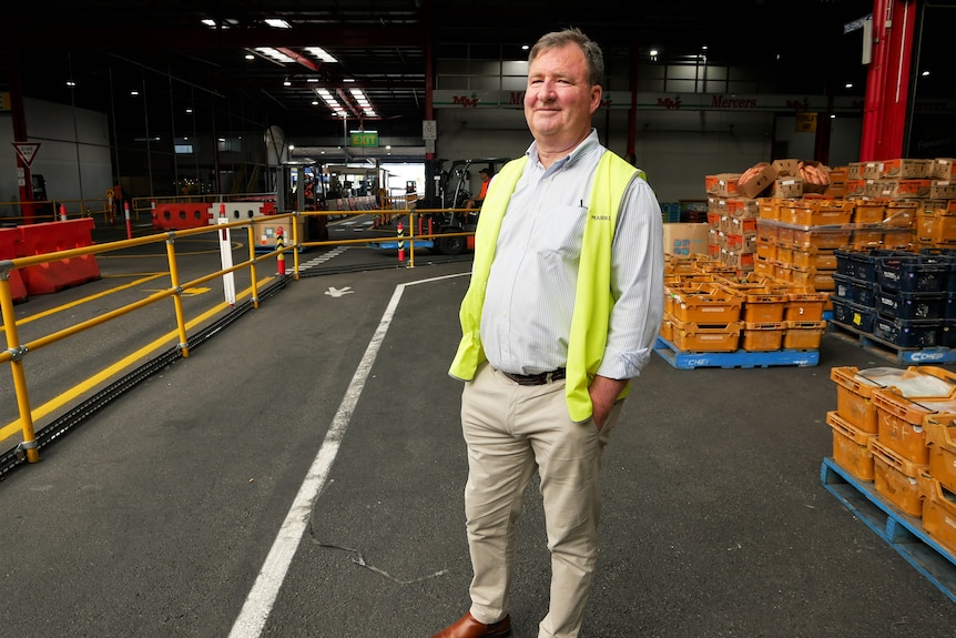 Man standing on concrete path with fruit crates behind.