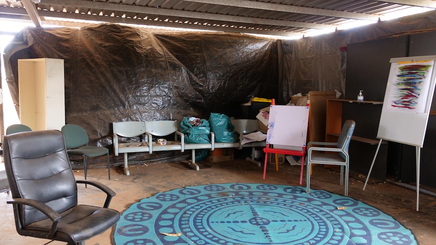 a meeting room with black tarp on windows and chairs around a mat