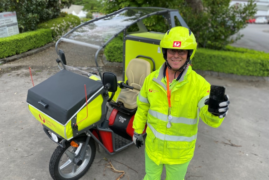 A man wearing hi-vis smiles at the camera while holding up a mobile phone. 
