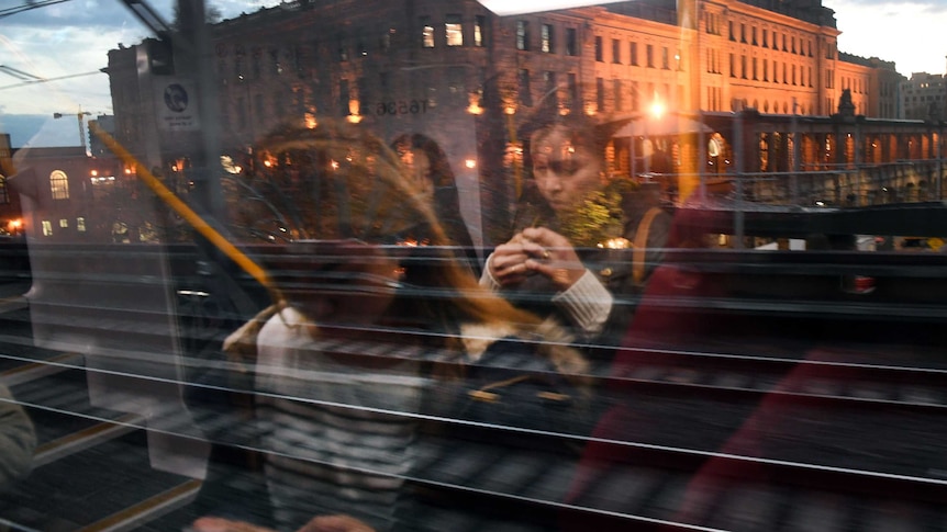 Women on their mobile phones are reflected in a train window.