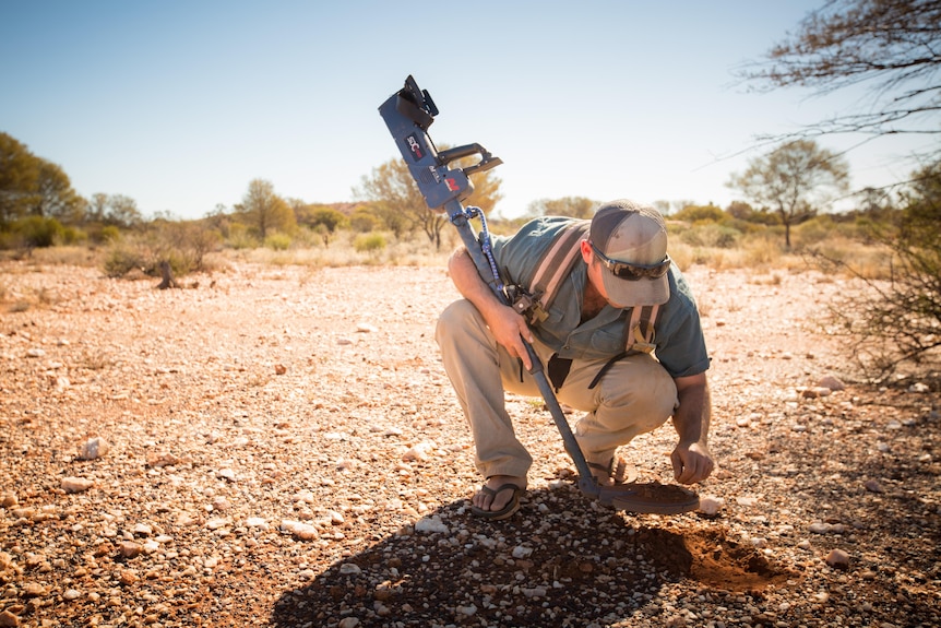 A man crouches on the ground with a metal detector.