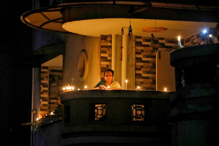 An older Indian woman on her balcony surrounded by candles