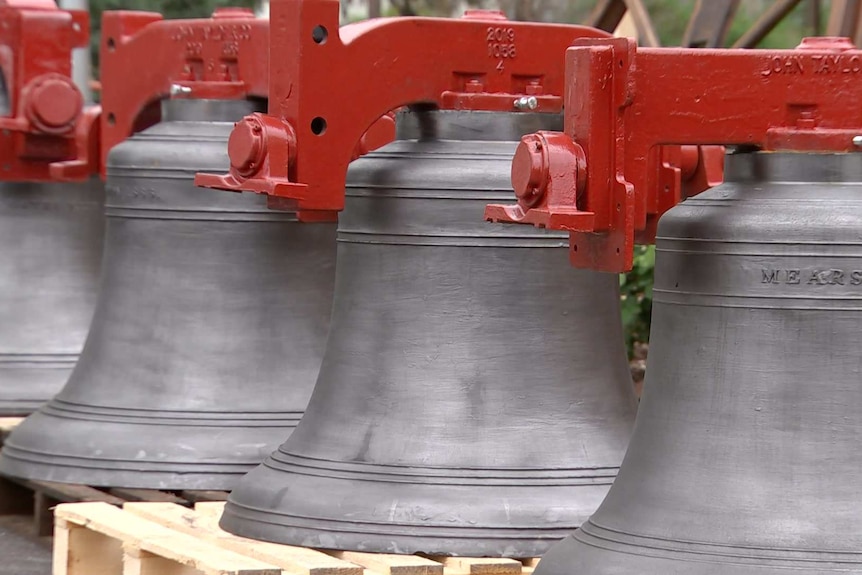 A row of large church silver bells under red yokes.