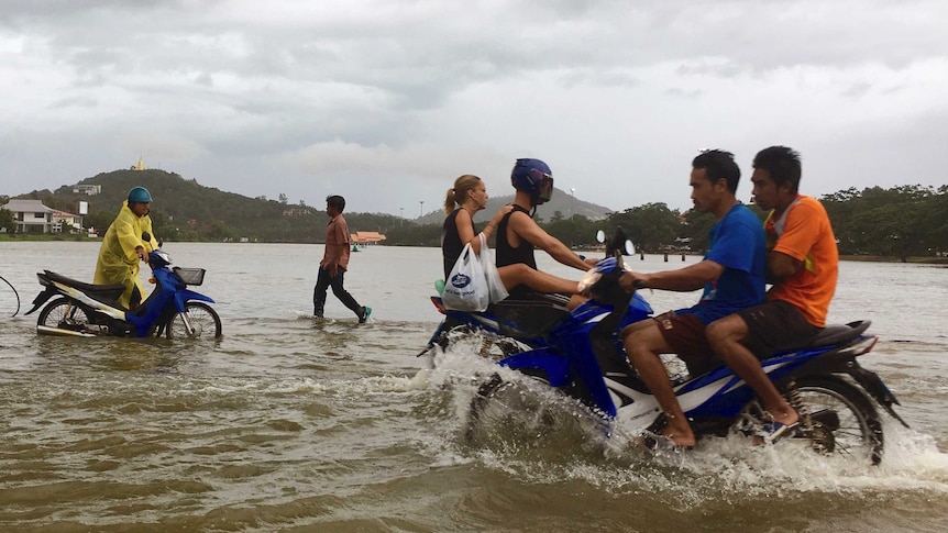 Pedestrians and people riding motorbikes traverse a flooded road in Thailand.