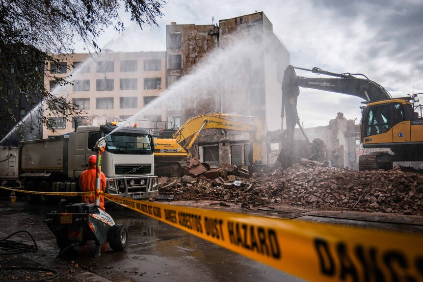 Large machinery and water vapour are used to clear rubble from the site.