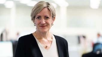 Clare Huppatz stands in an office looking at the camera.