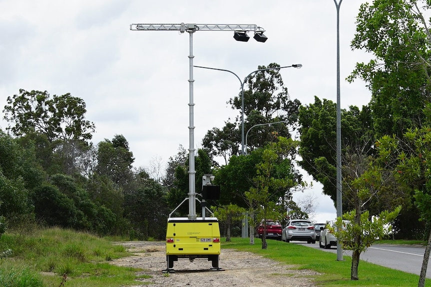 A wide shot of a mobile traffic camera on wheels, with cars visible on a road next to it
