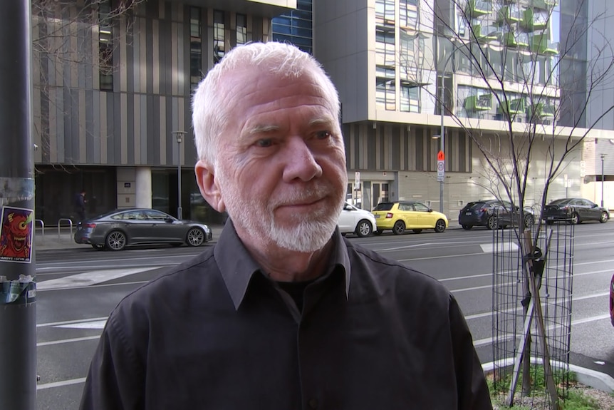 A man with grey hair and a beard standing in front of a road in Adelaide's CBD. 
