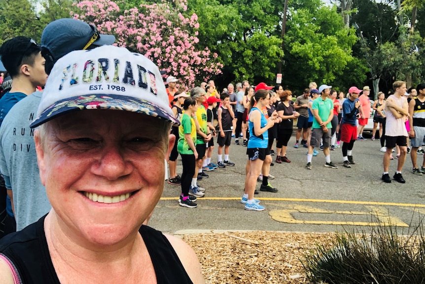 A woman smiles at the camera in a selfie with a crowd of runners behind