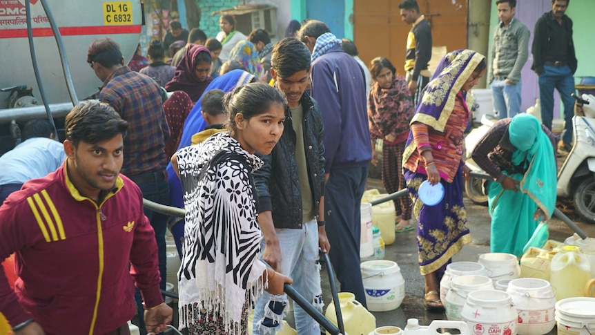 Men and women holding hoses and filling up their water containers from a water truck in Delhi.