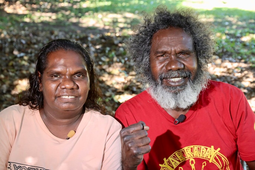 Two Indigenous people sit down and smile at camera