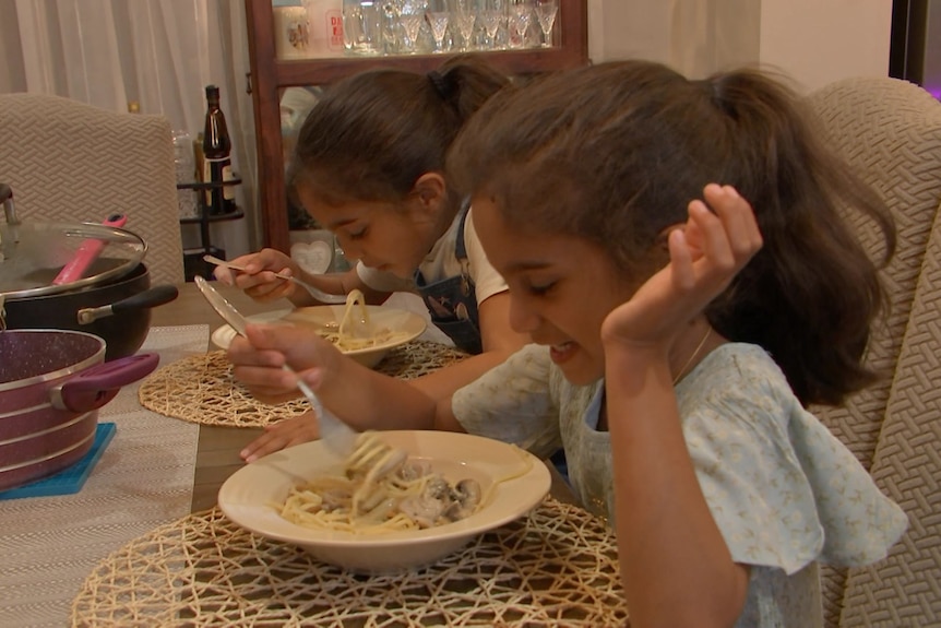 Twin girls eating pasta at a table.