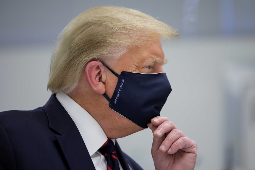 Donald Trump in profile wearing a dark mask with his hand on his chin