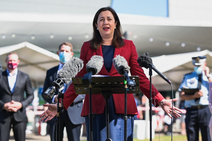 Annastacia Palaszczuk stands in front of microphones with her arms spread.