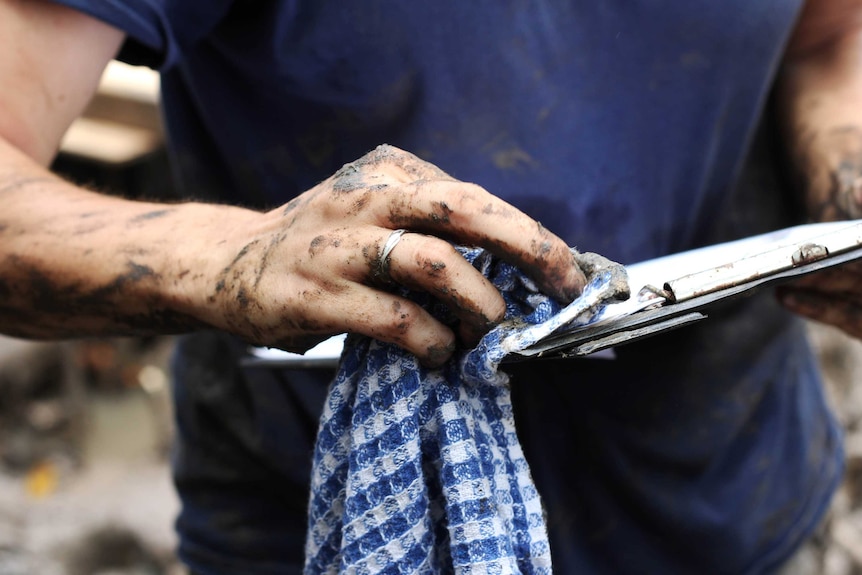 A woman's muddy hands wipe down a clipboard covered in mud.