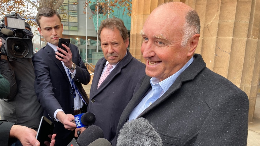 John Hanlon speaks into journalists' microphones outside a court building. 