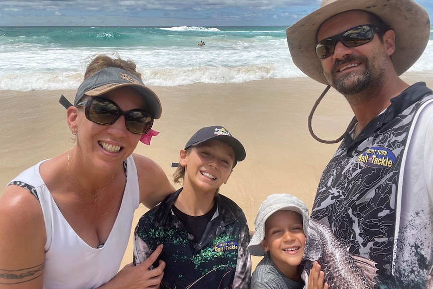 Mum, Dad and kids smiling, sand and beach waves behind them.