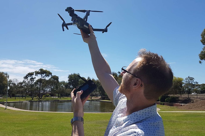 Teacher flies black drone in a tree filled park with a duck pond on a clear sunny day.