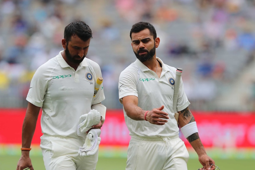 Indian batsmen Cheteshwar Pujara and Virat Kohli speak to each other as they walk off the field.