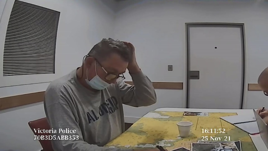 A still from a video shows Greg Lynn sitting at a desk in a police station.