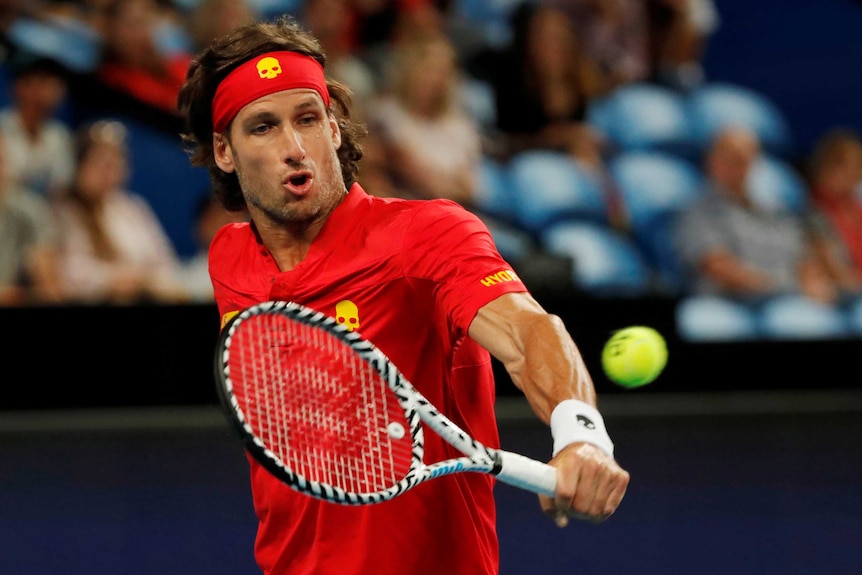 Lopez with a red headband and shirt with yellow skull hit a backhand.