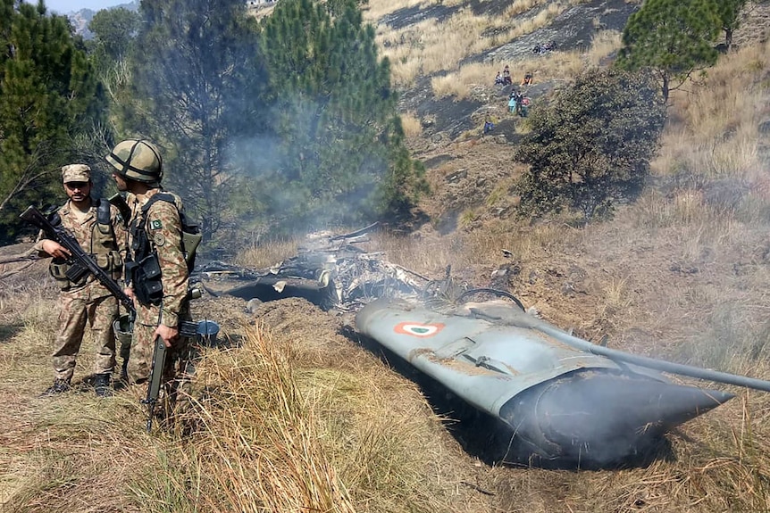 Pakistani soldiers surround the broken remains of an Indian fighter jet.