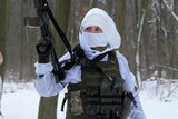 Members of Ukraine's Territorial Defence Forces wearing snow camo stand in a snowy wooded area in Kyiv, one holds a machine gun