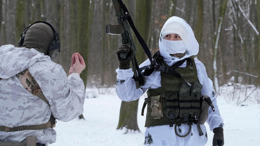Members of Ukraine's Territorial Defence Forces wearing snow camo stand in a snowy wooded area in Kyiv, one holds a machine gun