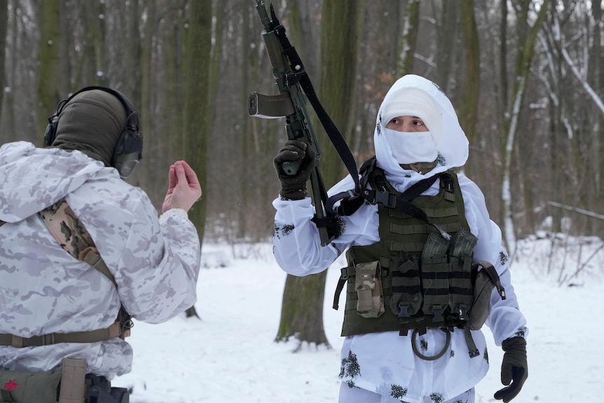 Members of Ukraine's Territorial Defence Forces wearing snow camo stand in a snowy wooded area in Kyiv, one holds a machine gun