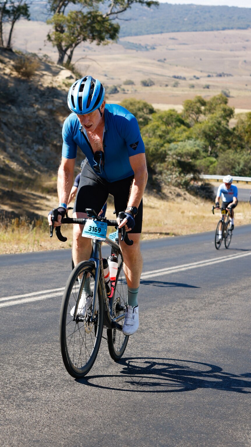 一位成熟的自行车手在比赛期间骑上山，他的赛车上衣拉链拉开。