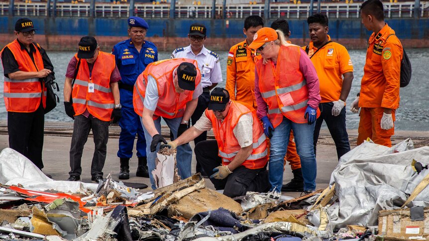 Investigators wearing hi-vis vests inspect wreckage from the Lion Air plane.