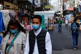 Two people wearing face masks walk down a street.