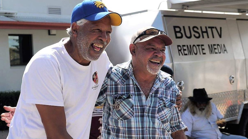 Ernie Dingo laughs while posing for a photo with another Indigenous man in front of BushTV truck