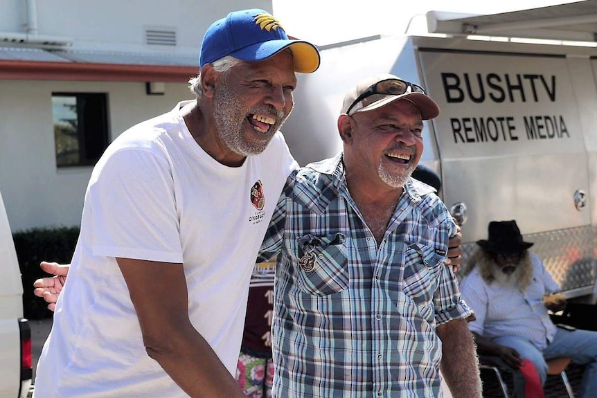 Ernie Dingo laughs while posing for a photo with another Indigenous man in front of BushTV truck