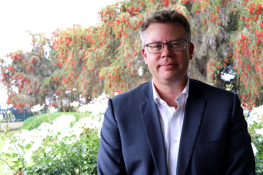 Evan Hall looks at the camera, standing in front of some native trees.