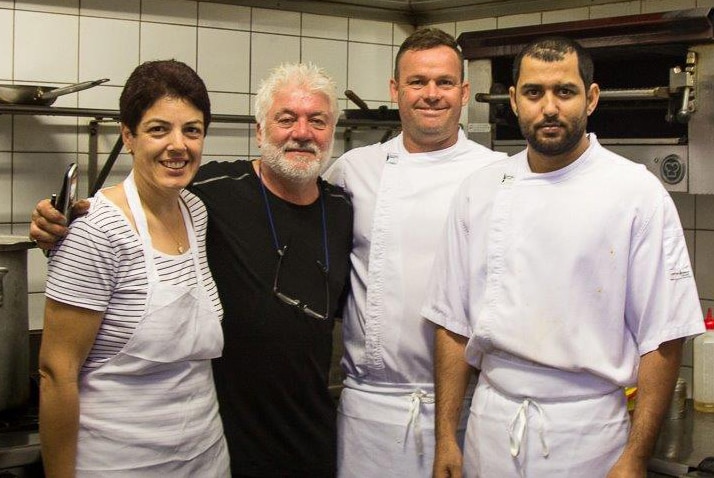 Four people including owner Enzo de Velta stand inside the kitchen of Romany Restaurant posing for a photo.