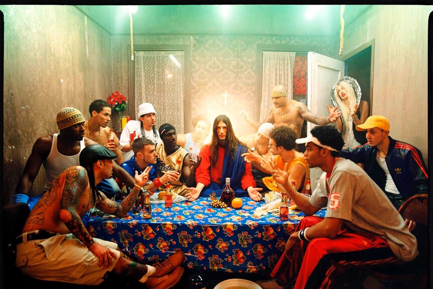 Jesus sits at a table surrounded by a dozen young men and women.