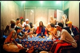Jesus sits at a table surrounded by a dozen young men and women.
