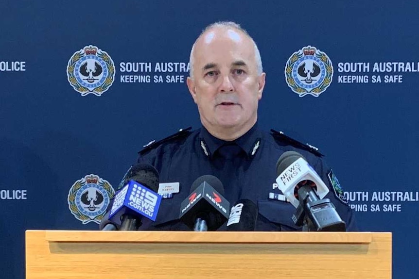A man in a police uniform standing in front of a board with SA Police logos