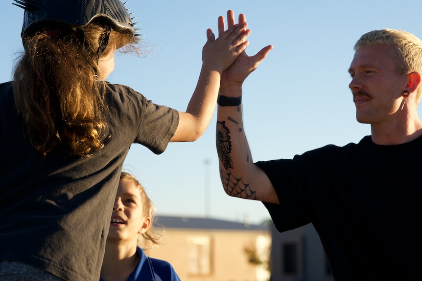Jayden Sheridan high fives a young girl wearing a helmet at the skatepark.