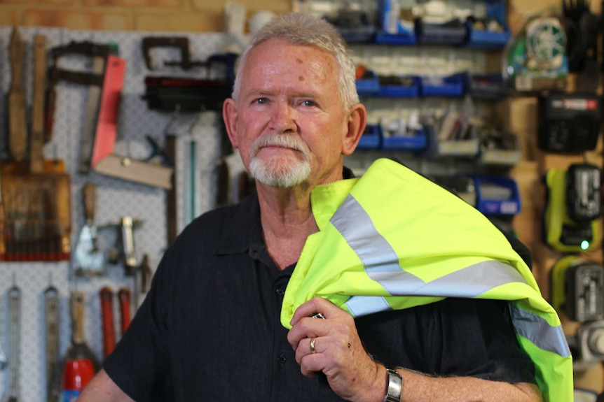 Max Green standing in his shed with high viz jacked on his shoulder and tools on the wall in background