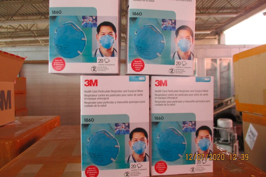 Four boxes of counterfeit medical-grade face masks are stacked on top of boxes in a warehouse.