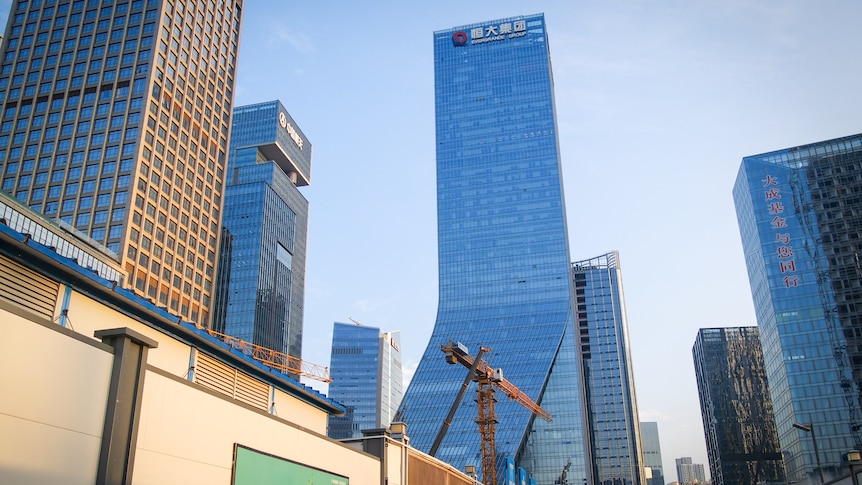A building soaring into a blue sky, with a crane in front of it 