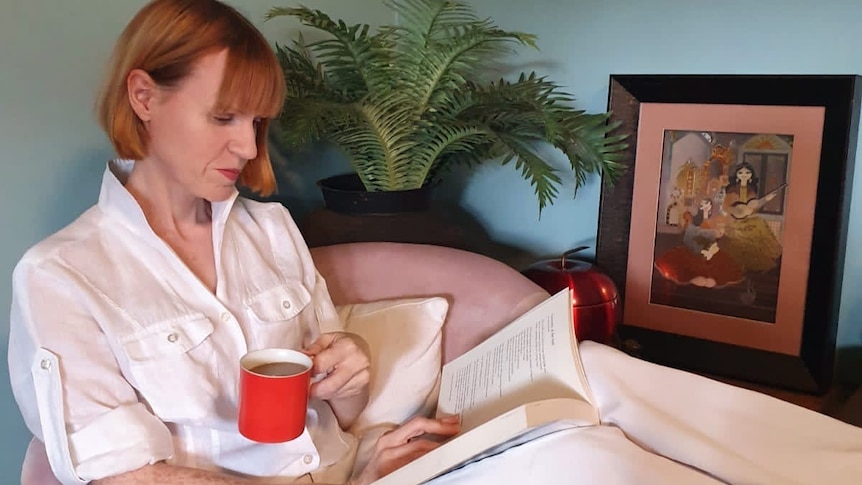 A woman sits on a chair with her feet up, a cup of tea and a book for a story on being the carer of a child with special needs