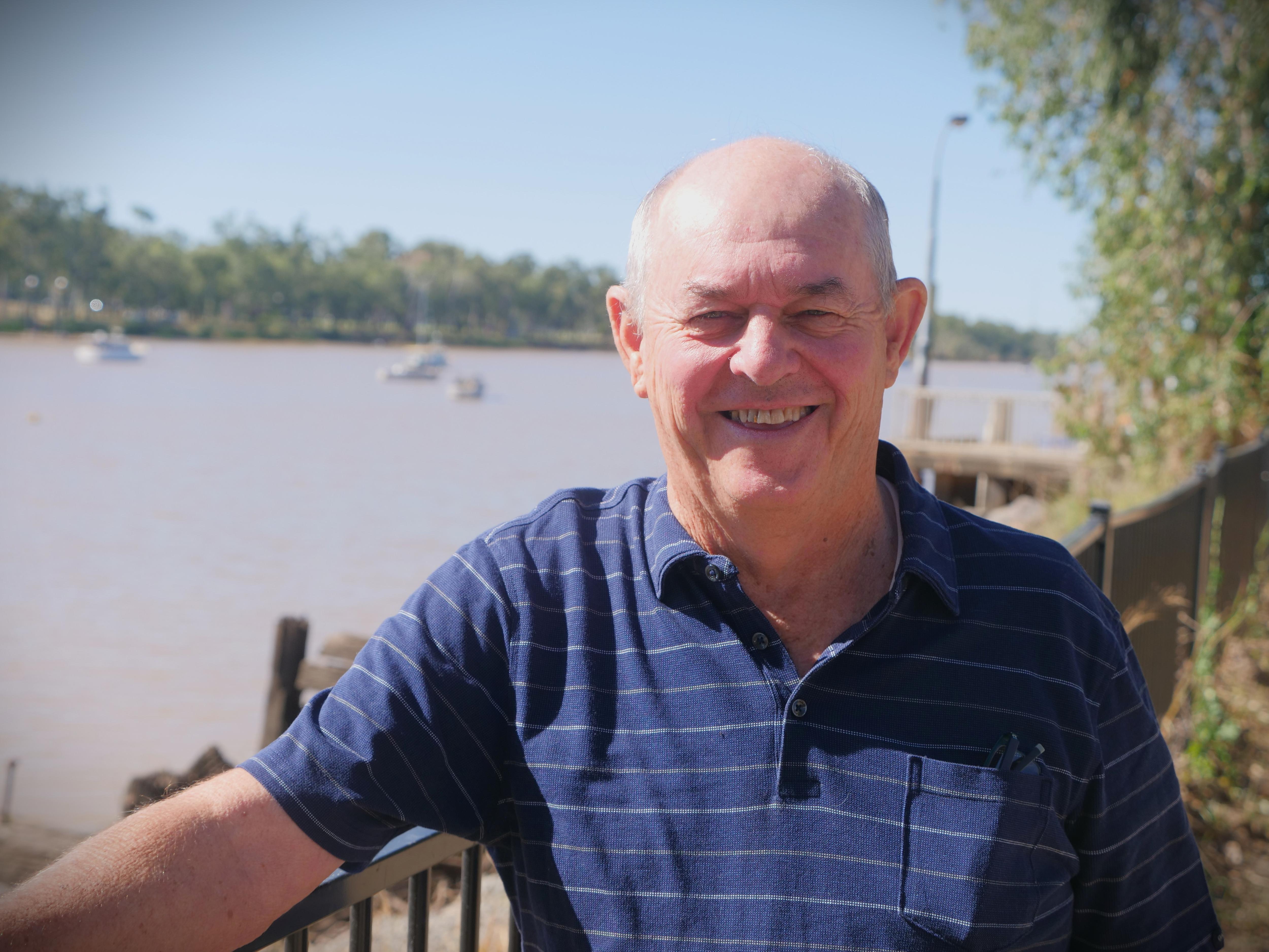 A man in a blue shirt smiles as he stands near a river.