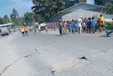 Cracks in the road in front of people standing in distance in rural jungle setting