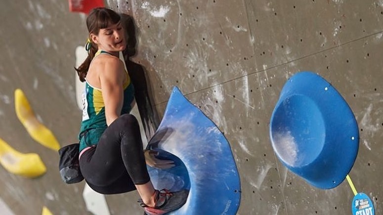 Girl in Australian colours climbs a rock-climbing wall.