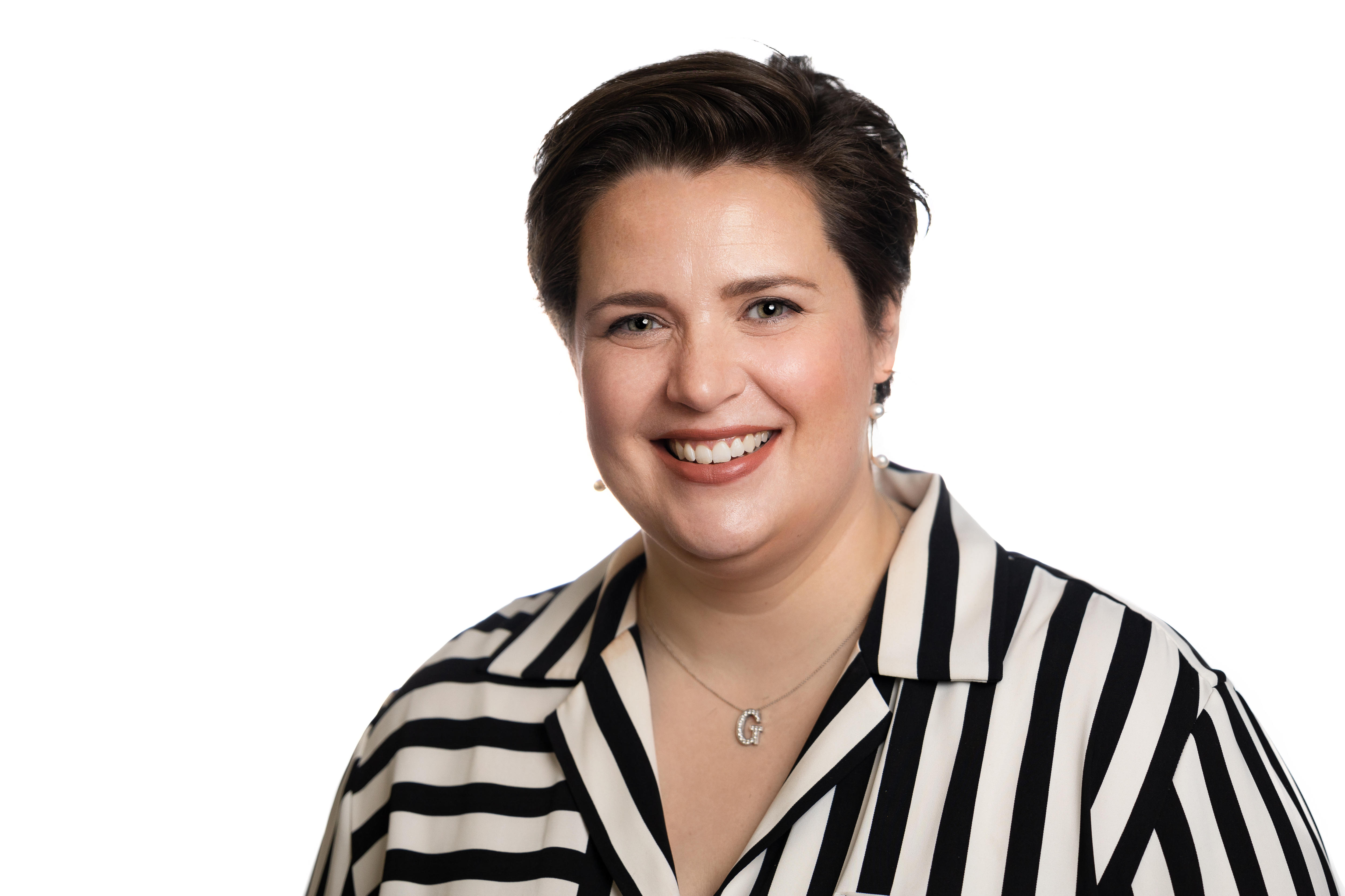 A woman with short brown hair, wearing a black and white striped shirt, smiles.